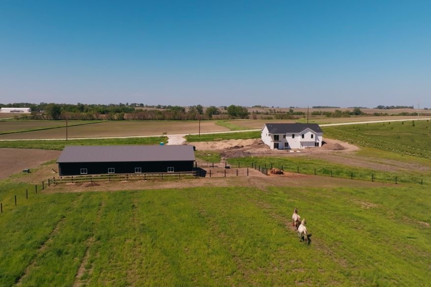 Custom Iowa home under construction on a rural acreage at golden hour, with framing, gravel drive, and surrounding fields.